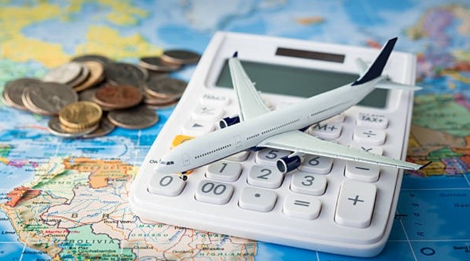 بنر - هزینه های سفر - یک ماکت هواپیما روی ماشین حساب سفید رنگ که روی نقشه کره زمین در کنار چند سکه پول قرار گرفته